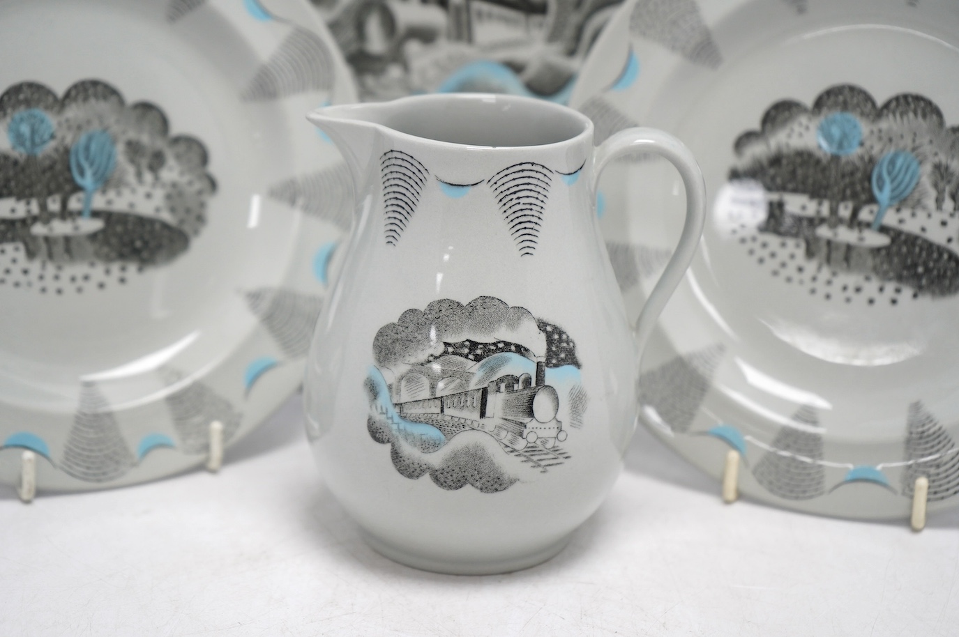 Four Wedgwood pottery items; all Travel pattern designed by Ravilious, comprising a small jug, 11.5cm high, and three plates. Condition - fair to good, minor marks and one chip to the jug only